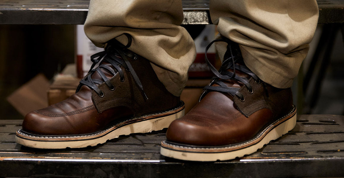 A person wearing a pair of brown boots standing on a ladder.