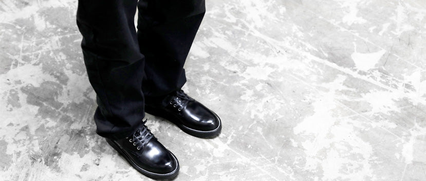 A person standing on a concrete floor wearing black shoes.