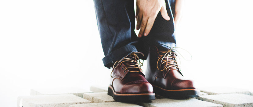 A pair of black leather boots with orange stitching and lace-up design, one standing and the other lying on its side.