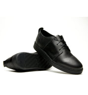 A pair of Broken Homme Ben Low black leather sneakers with a cork filled midsole on a white background.